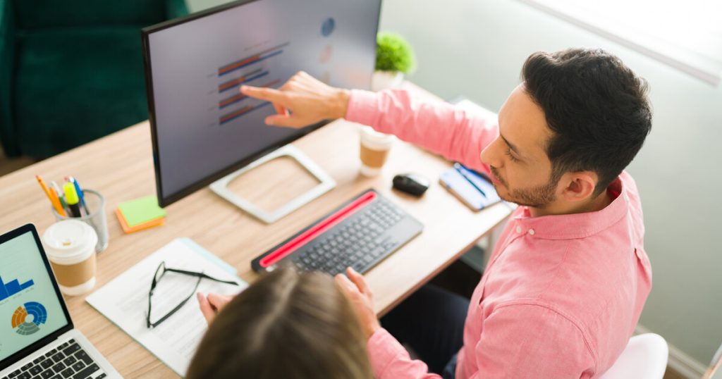 Two colleagues reviewing data on a monitor while planning an A/B test step by step